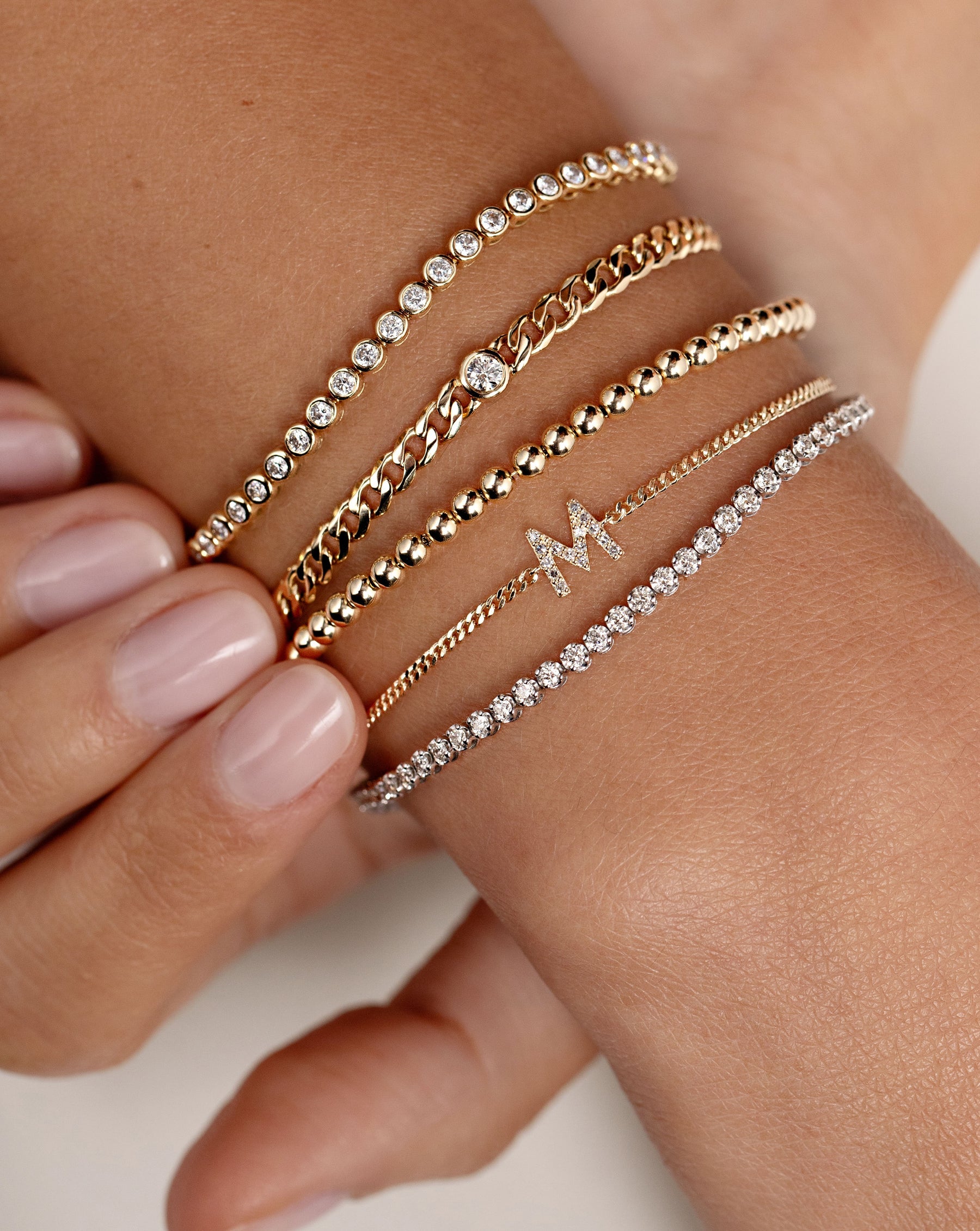 bezel-set classic diamond tennis bracelet, petite bezel-set diamond curb chain bracelet, gold bead bracelet, pave initial bracelet, and mini diamond tennis bracelet on model