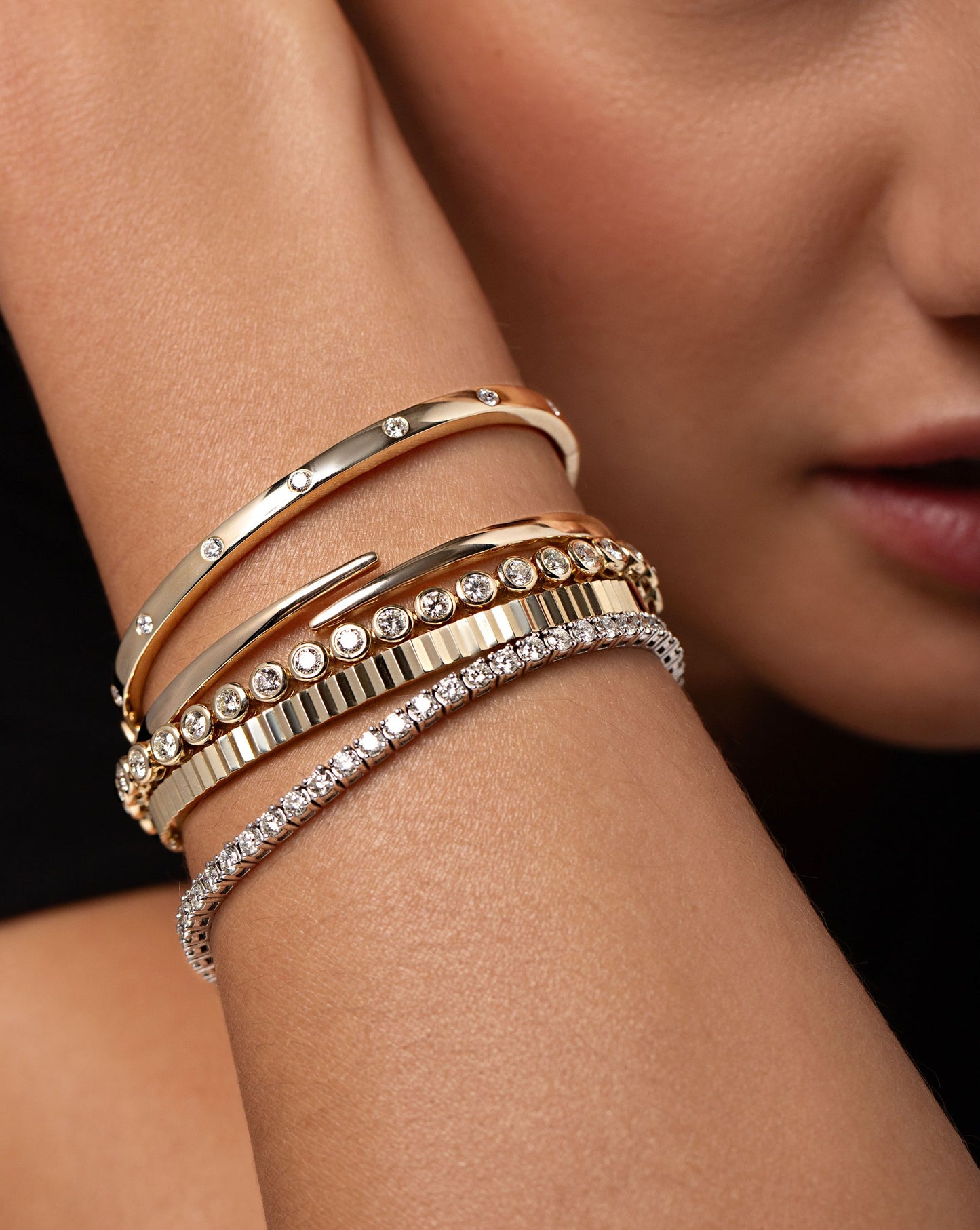 Close up of the Open Gold Wrap Bangle styled on wrist with the Fluted Gold Bangle, Inlay Diamond Bangle, Classic Diamond Tennis Bracelet and the Bezel Set Classic Diamond Tennis Bracelet