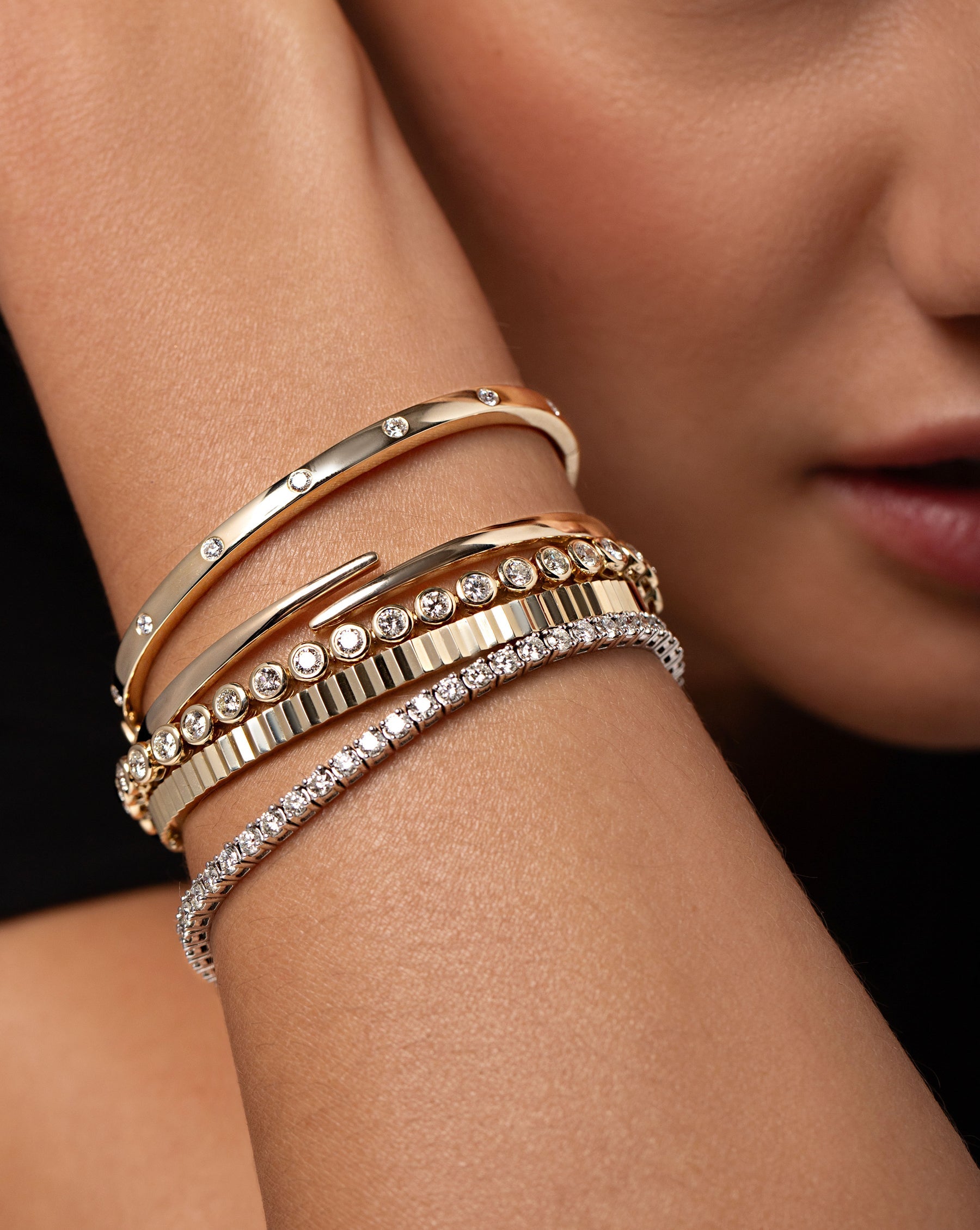 Close up of the Open Gold Wrap Bangle styled on wrist with the Fluted Gold Bangle, Inlay Diamond Bangle, Classic Diamond Tennis Bracelet and the Bezel Set Classic Diamond Tennis Bracelet