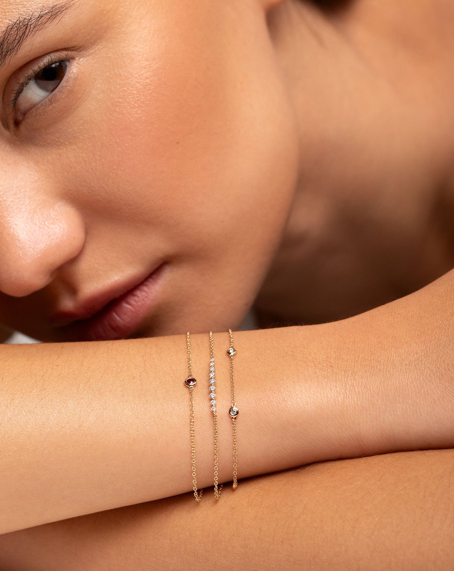 Graduated Single Prong Diamond Bracelet in 14kt yellow gold shown styled with the Gemstone Bezel Set Bracelet and the Diamond Bezel Set Station Bracelet on wrist of model with arm by face
