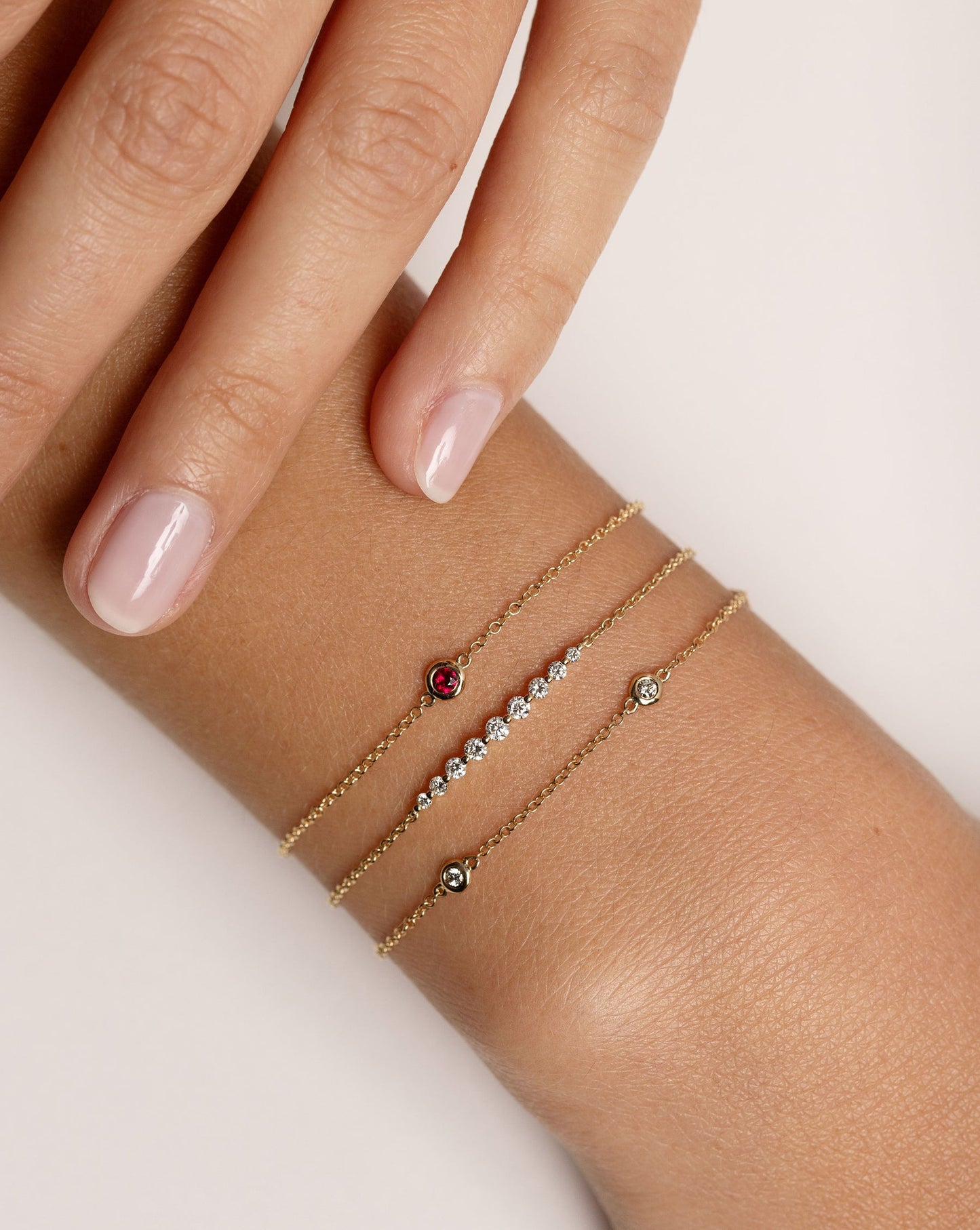 bezel-set ruby bracelet with gold chain, graduated diamonds on chain bracelet, and bezel-set round diamond station bracelet shown on model