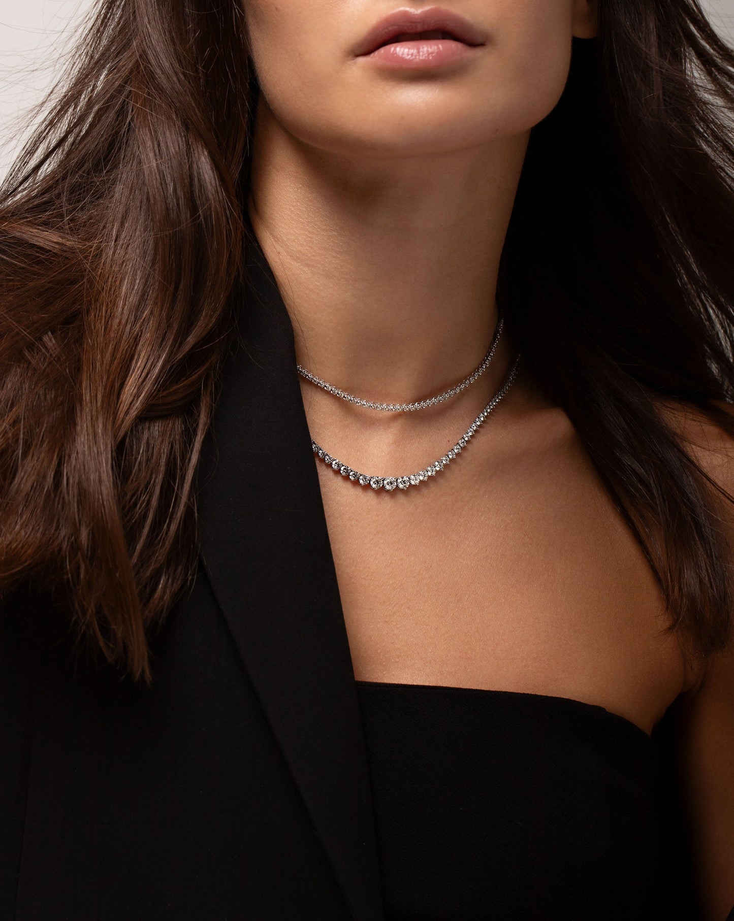 Model wearing multiway tennis necklace + double wrap bracelet and graduated tennis necklace with blazer over shoulder