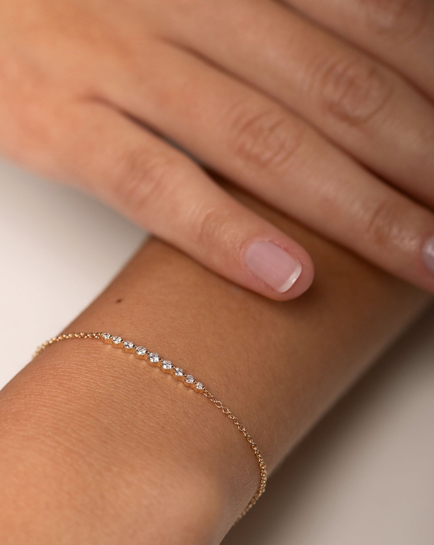 Graduated Single Prong Diamond Bracelet in 14kt yellow gold shown on wrist with other hand resting near the bracelet