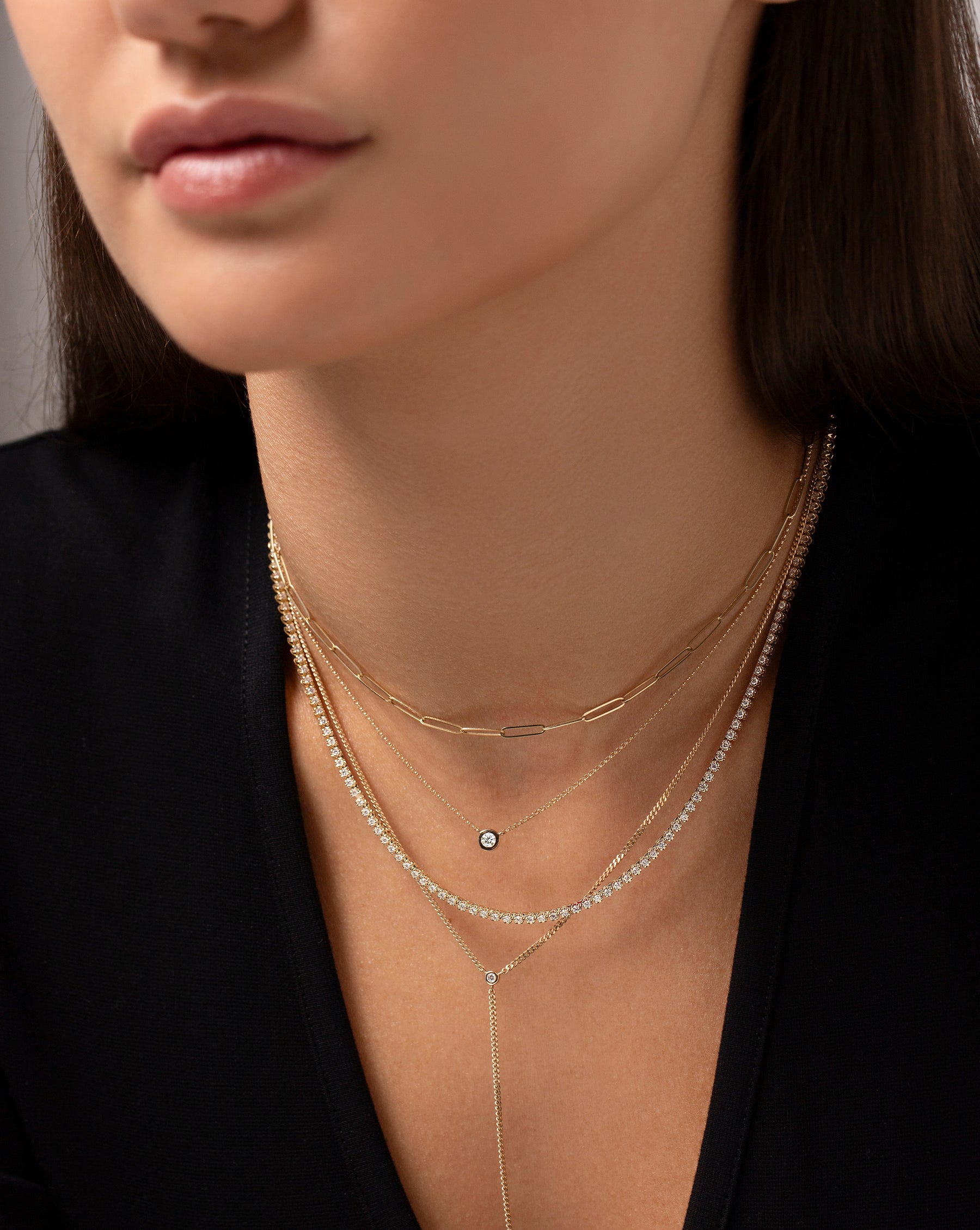 14k yellow gold link chain necklace, bezel-set round diamond pendant necklace, classic diamond tennis necklace, and lariat chain necklace shown on model