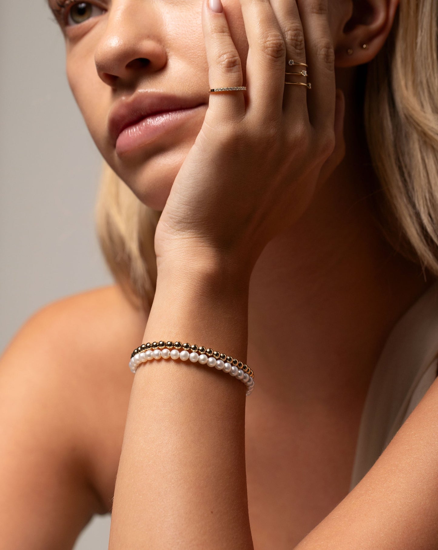 Multiway Pearl and Gold Beaded Necklace + Double Wrap Bracelet worn double wrapped around wrist with hand resting on face of model 
