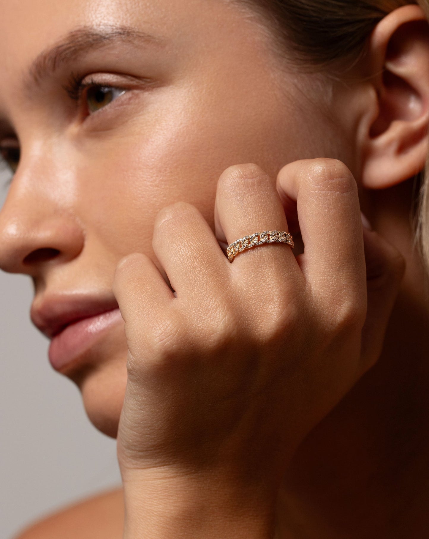 Pavé Diamond Chain Ring in 14k yellow gold worn on middle finger of hand resting on face