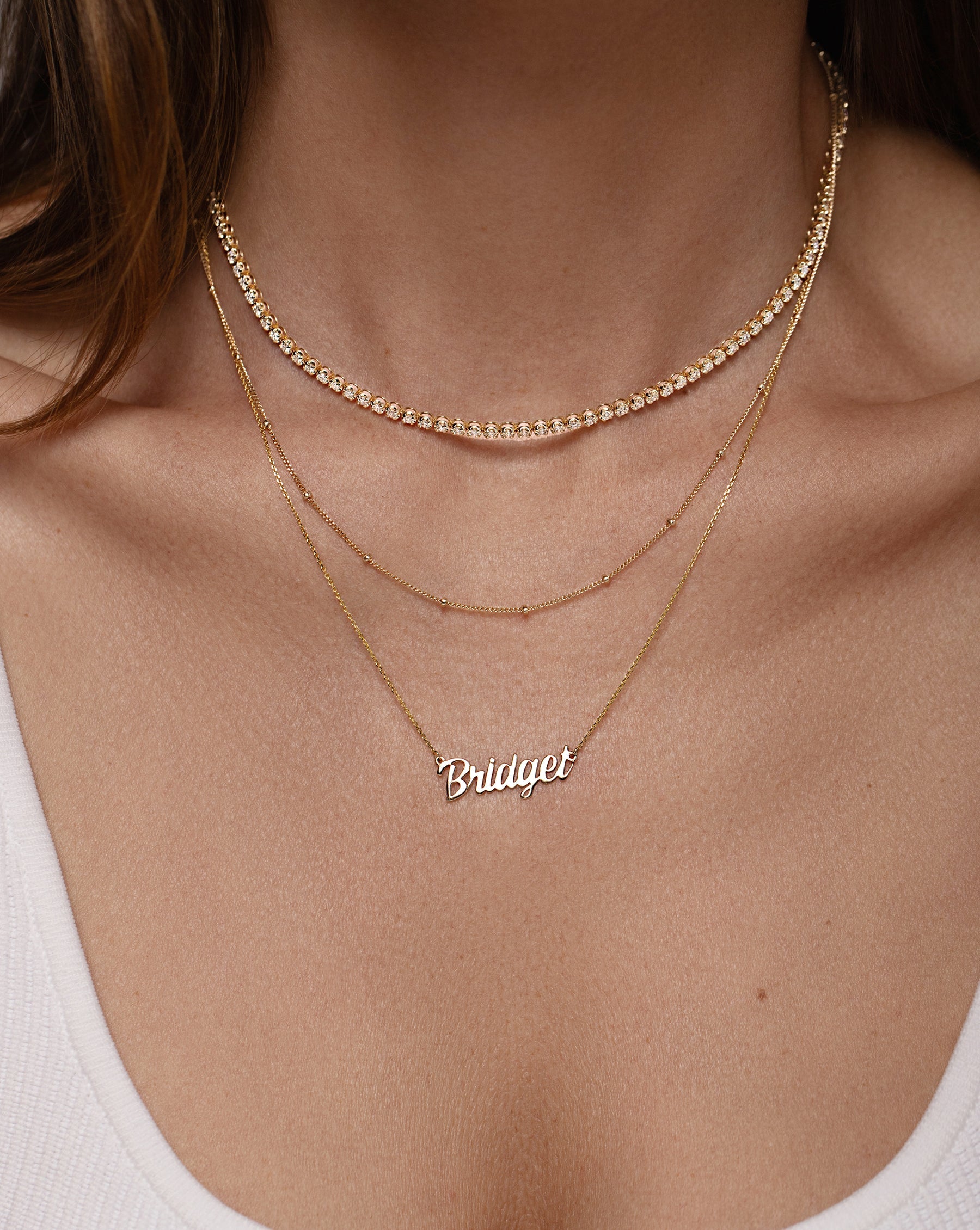 14k yellow gold necklace with the name Bridget in script font, gold bead station necklace, and cupcake set diamond tennis necklace shown on model