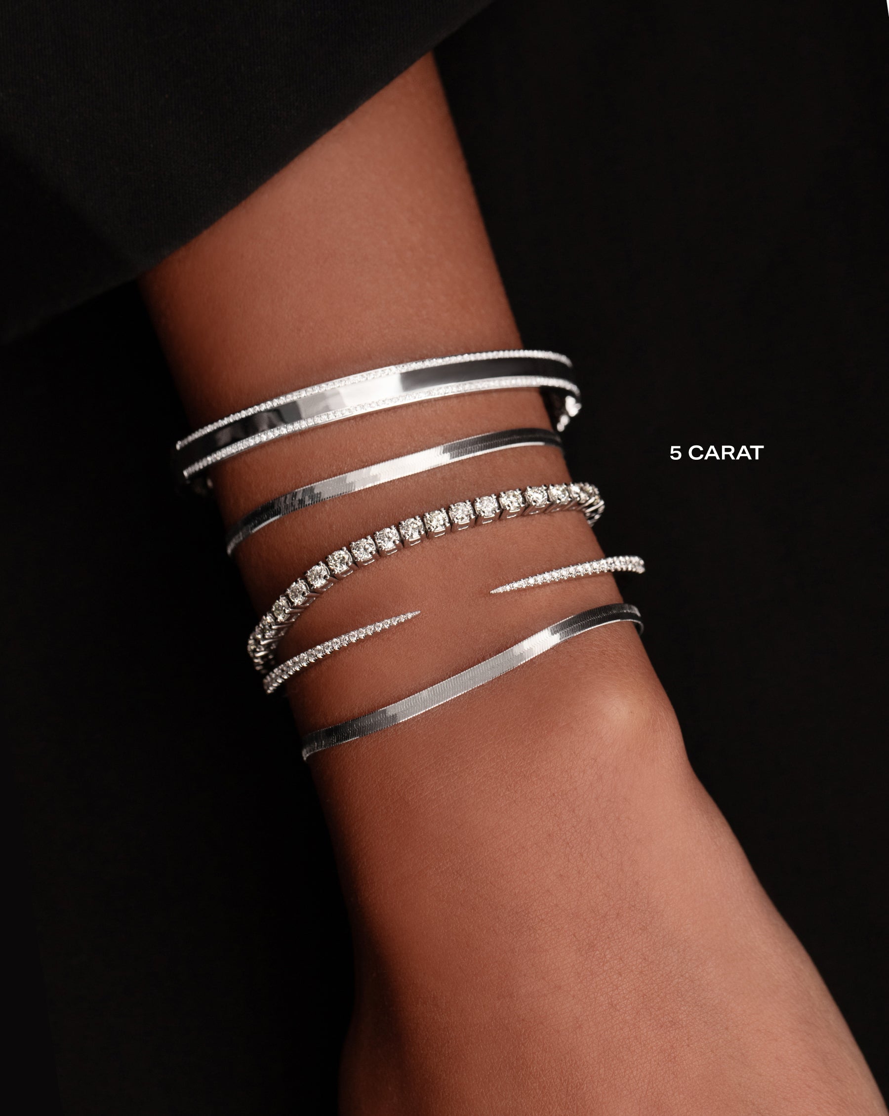gold and diamond border bangle, white gold herringbone bracelet, five carat classic diamond tennis bracelet, gold claw cuff, and white gold herringbone bracelet on model
