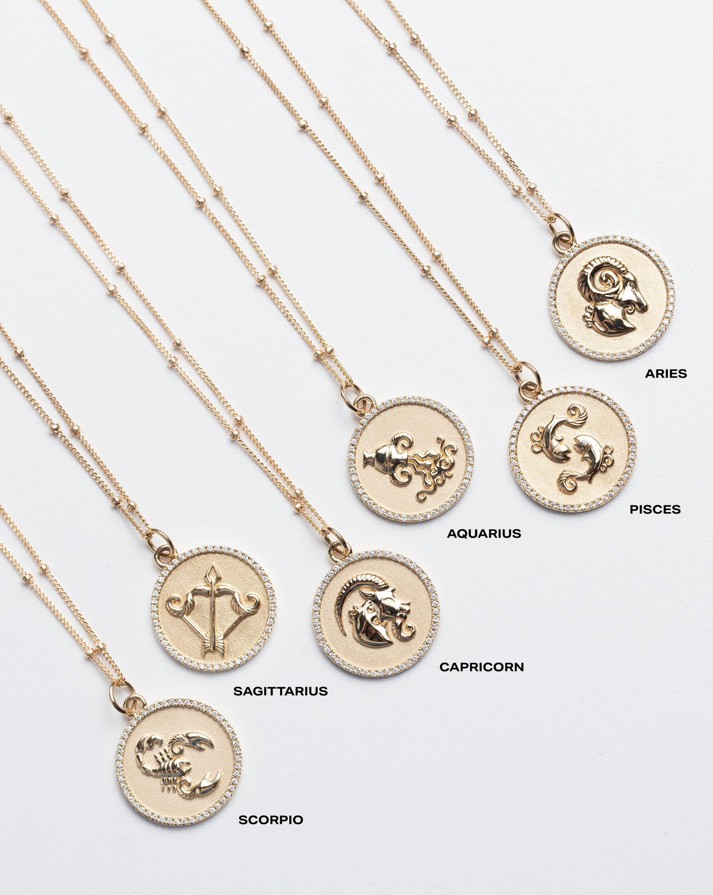 Flat lay of Zodiac Medallion Necklaces including Scorpio, Sagittarius, Capricorn, Aquarius, Pisces and Aries