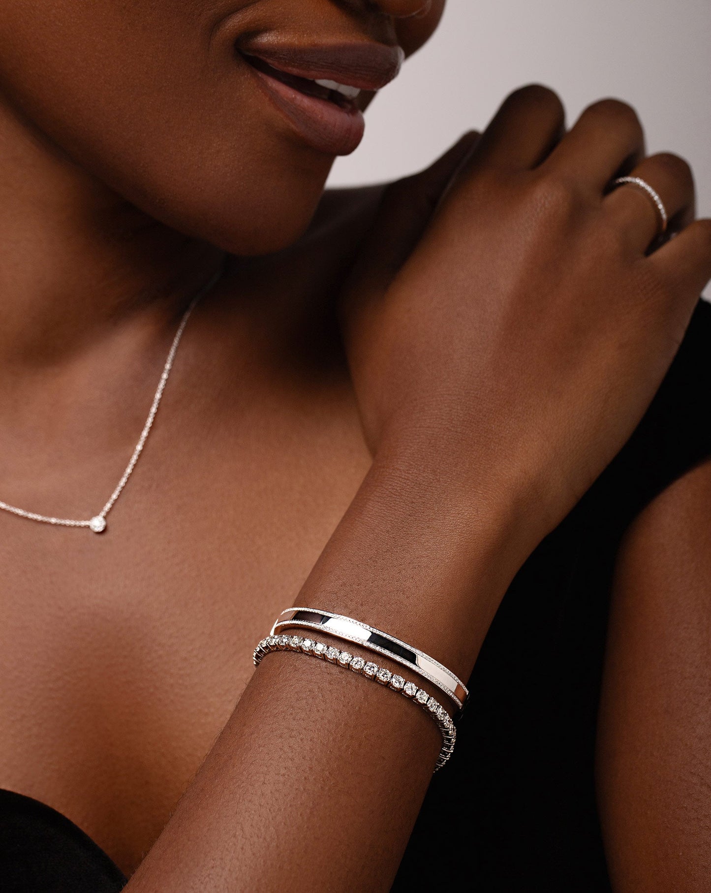 diamond cluster pendant necklace, 14k white gold bangle with diamond border, and bezel-set round diamond tennis bracelet shown on model