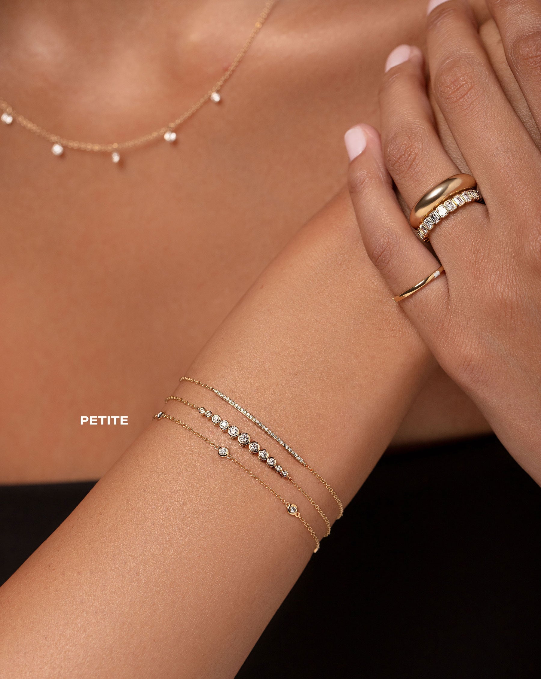floating diamond necklace, petite bezel-set round diamond station bracelet, bezel-set round graduated diamond bracelet, diamond bar bracelet, gold pinky ring, bezel-set emerald diamond eternity band, and gold cloud ring show on model
