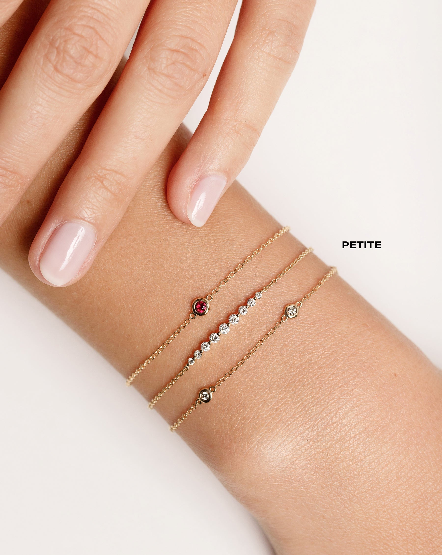 bezel-set ruby bracelet with gold chain, graduated diamonds on chain bracelet, and bezel-set round diamond station bracelet shown on model