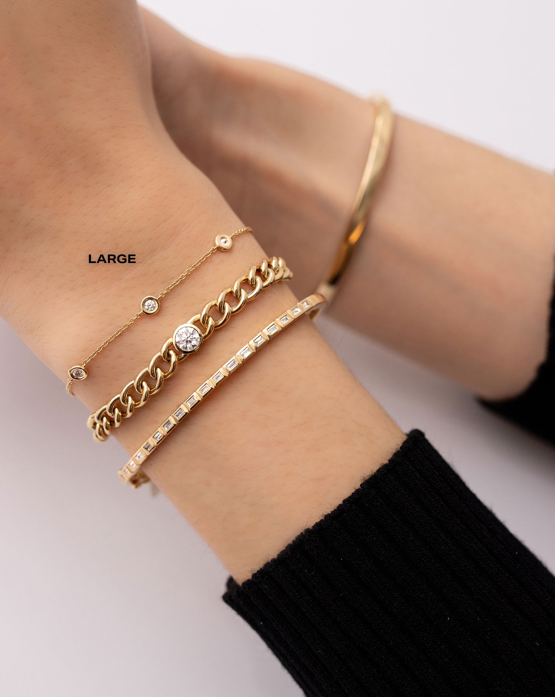 petite bezel-set round diamond station bracelet, gold curb chain bracelet with bezel-set round diamond, and bezel-set baguette diamond bangle shown on model