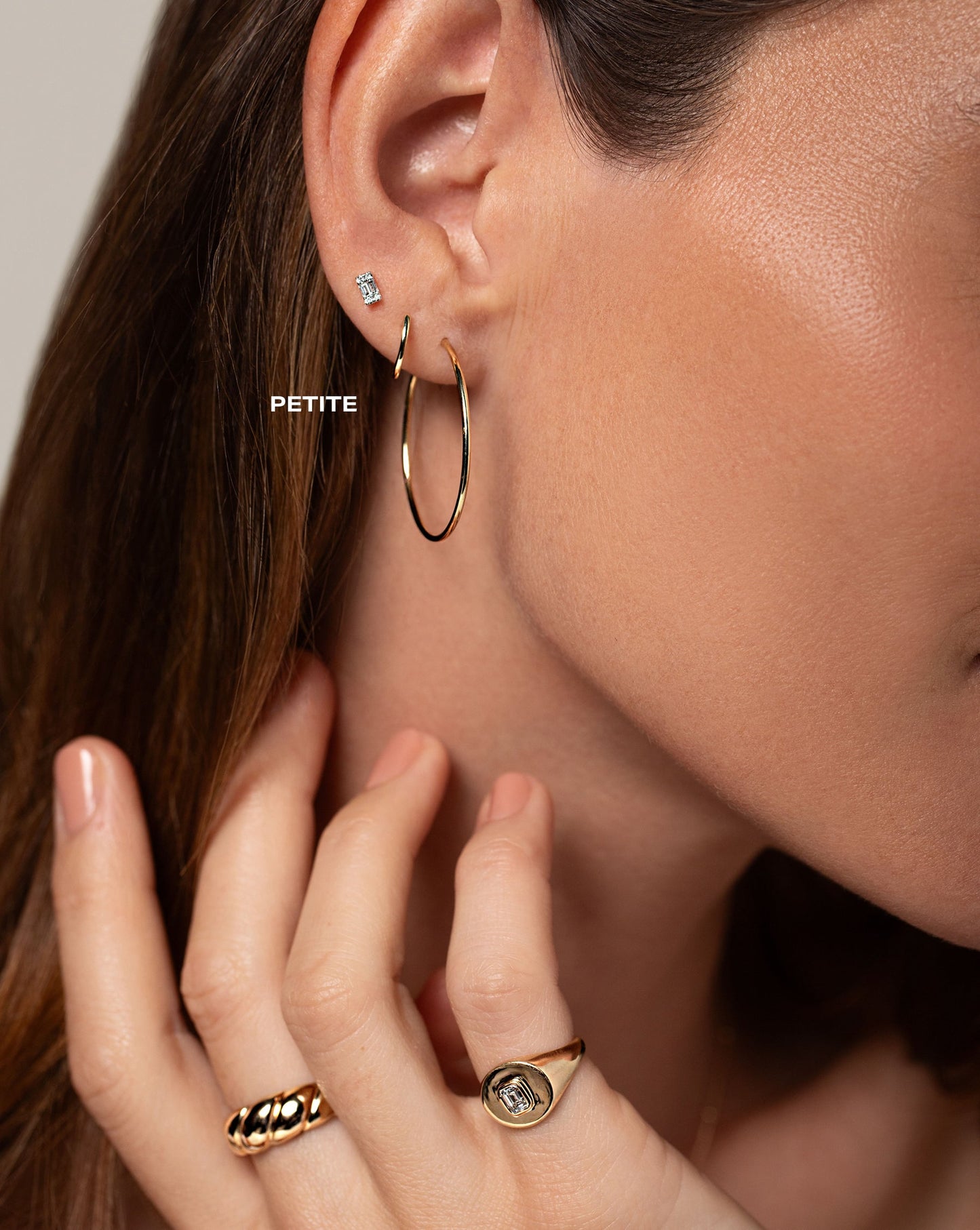 mini diamond emerald illusion stud, classic gold huggie, medium size of 1mm gold tube hoops, golden croissant ring, and gold signet pinky with with emerald-cut diamond shown on model