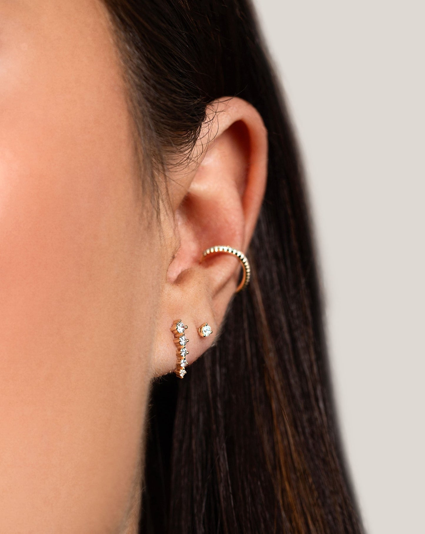 Graduated Curved Studs styled with tiny diamond studs and diamond ear cuff on model at an angled shot