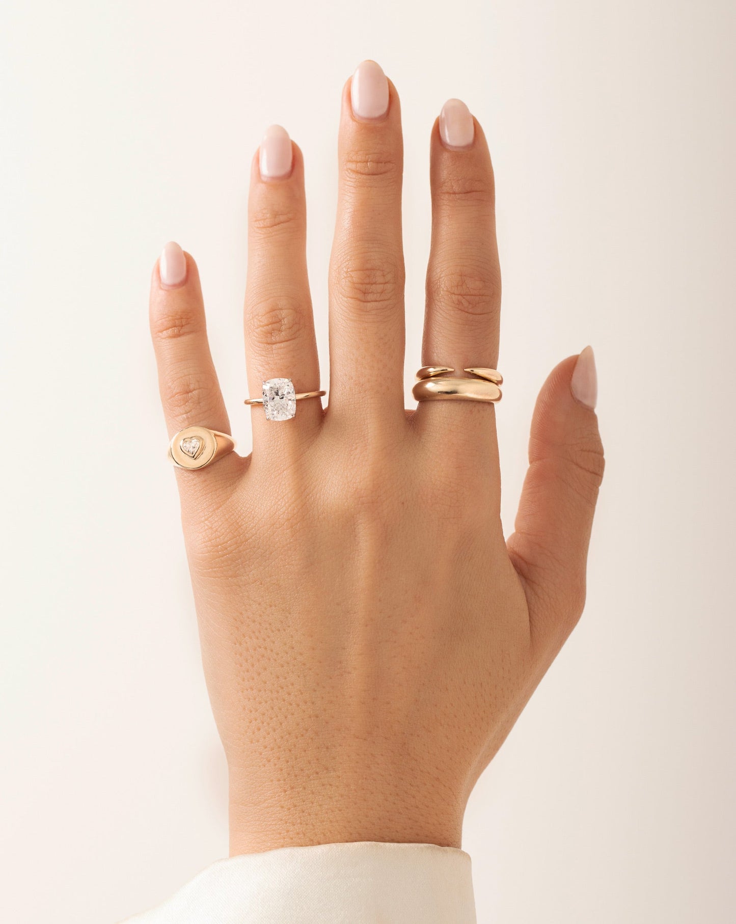 Gold signet pinky ring with heart-cut inlay diamond, radiant-cut diamond engagement ring, gold claw stackable ring, and gold cloud ring shown on model