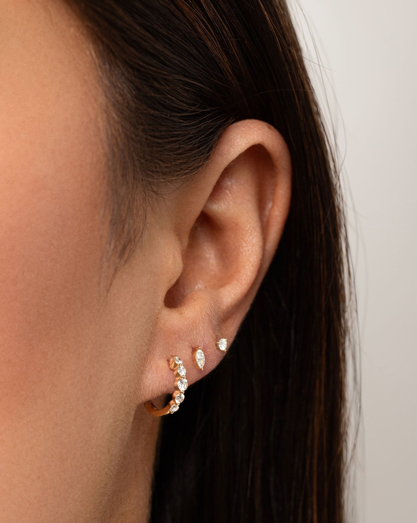 Graduated Single Prong Diamond Huggies styled on model with tiny marquise stud and tiny diamond stud at an angled shot