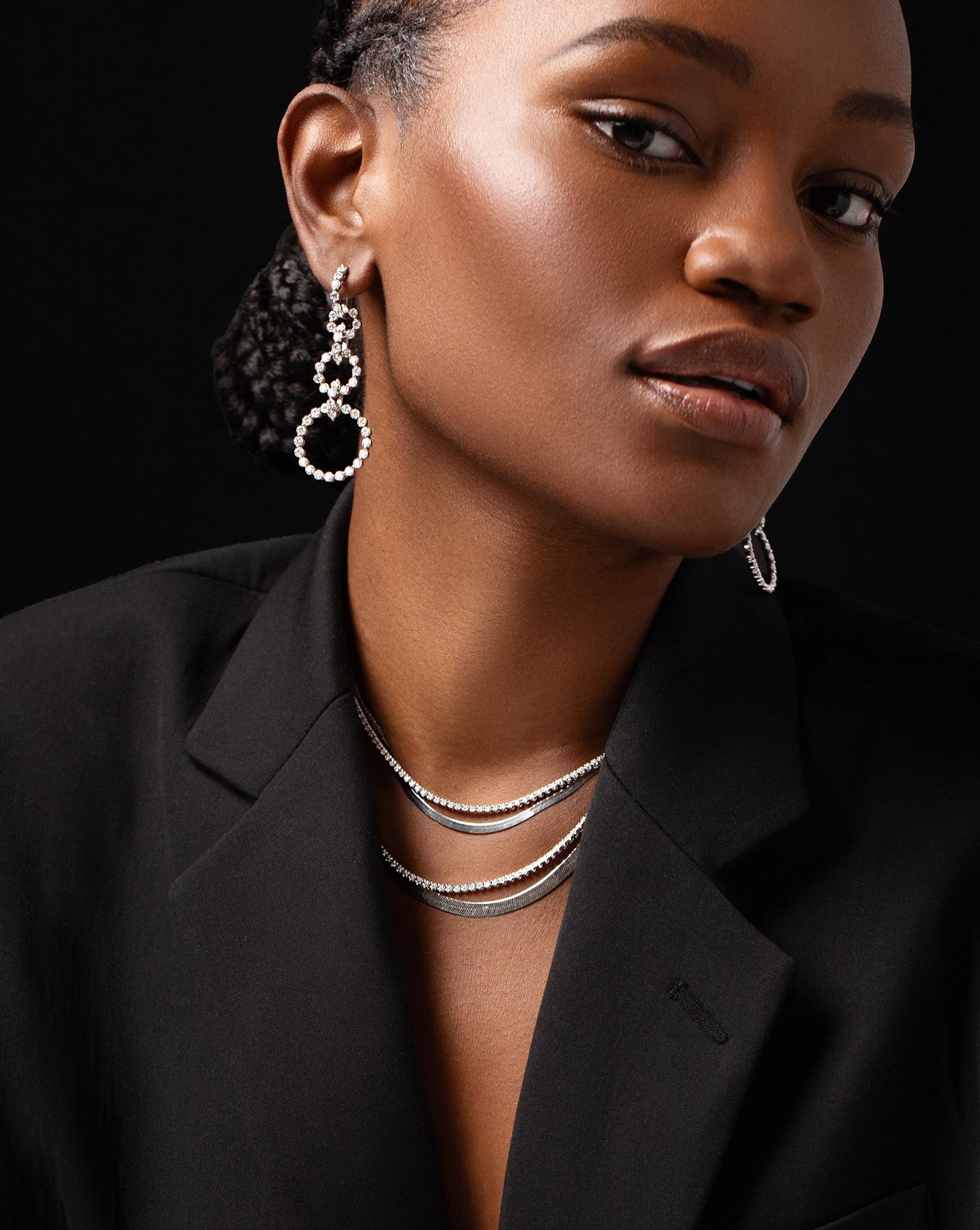 diamond statement earrings featuring three graduated circle drop hoops, two diamond tennis necklaces and two white gold herringbone chain necklaces a shown on model