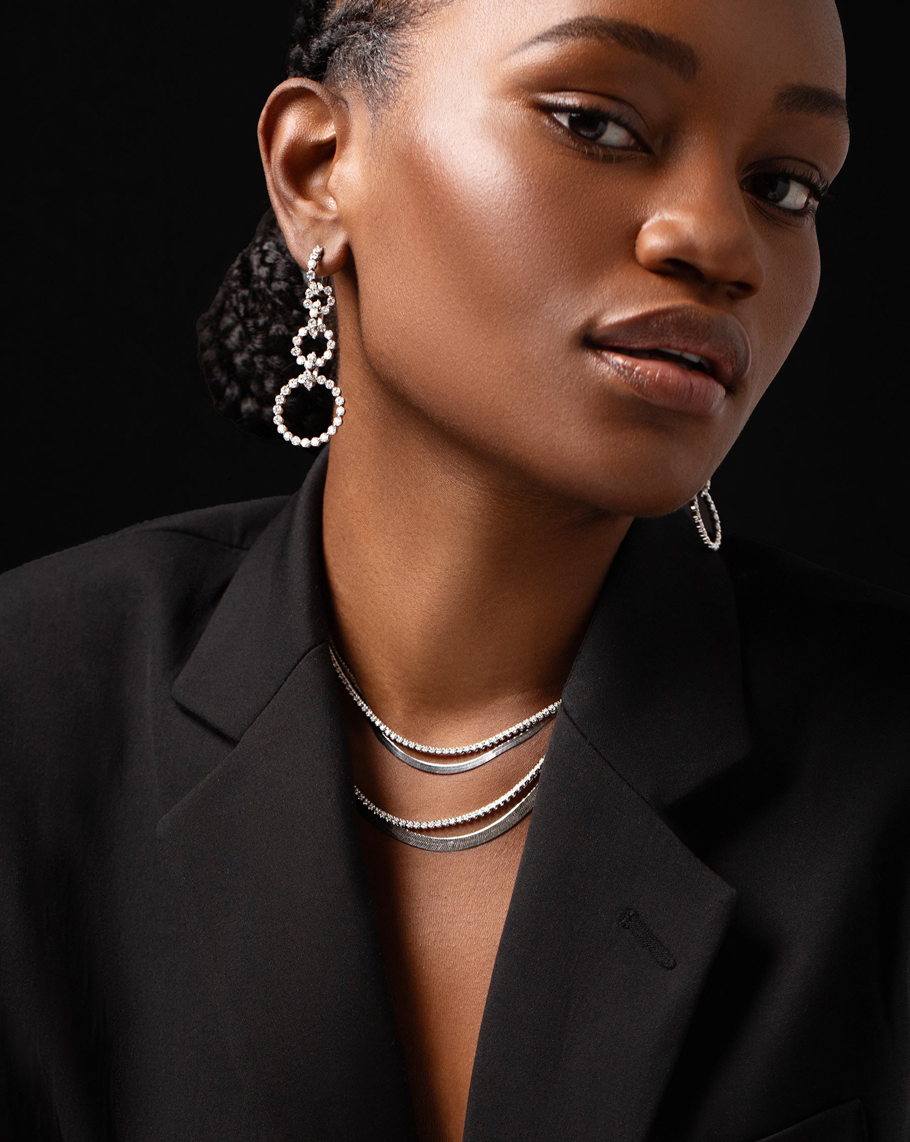 diamond statement earrings featuring three graduated circle drop hoops, two diamond tennis necklaces and two white gold herringbone chain necklaces a shown on model