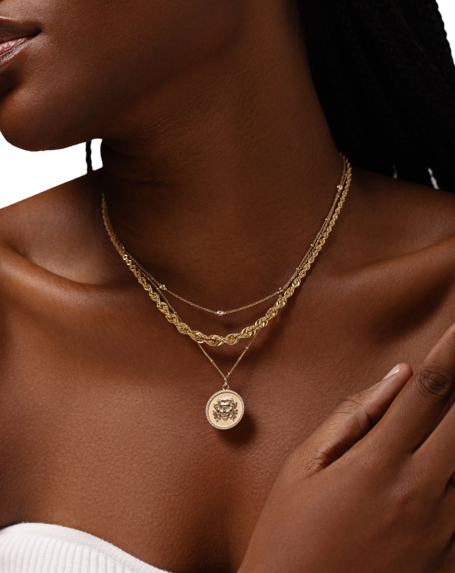 bezel set round diamond station necklace, gold rope chain necklace, and zodiac medallion necklace on model