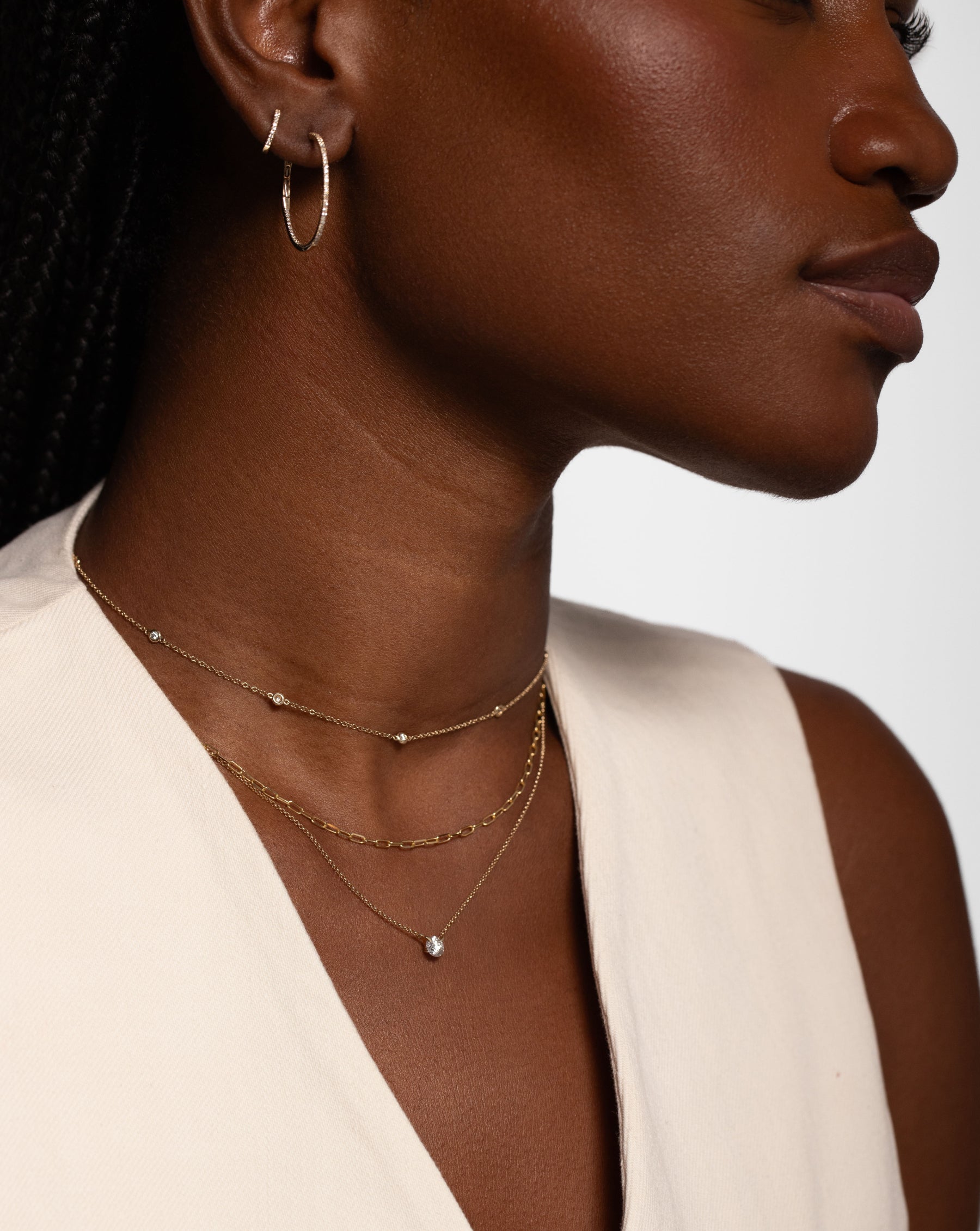 one small diamond hoop, one large diamond hoop, bezel set round diamond station necklace, small gold link chain necklace, and single diamond pendant necklace on model