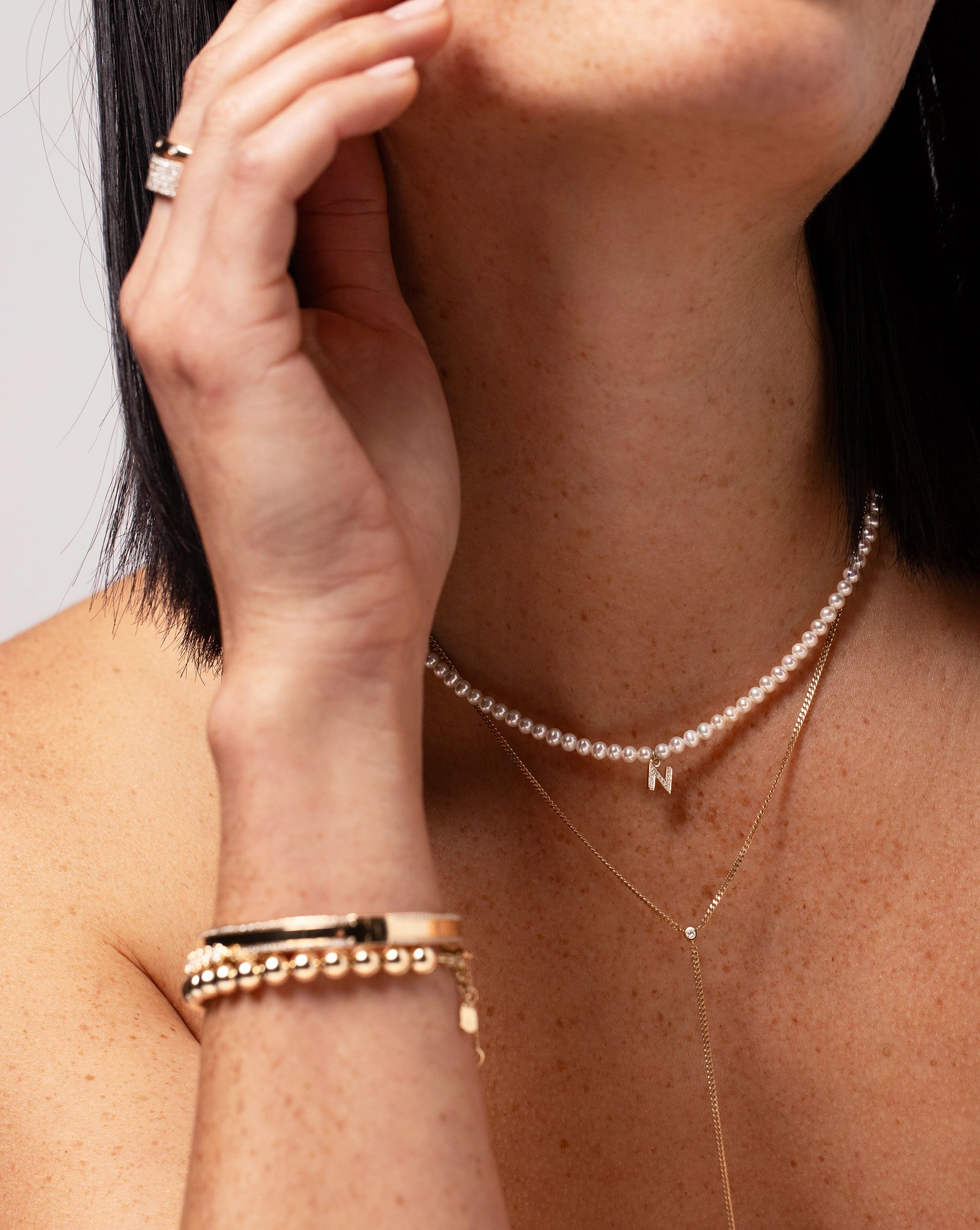 Pearl + Pavé Initial Choker letter N shown around neck of model with the Diamond Cut Curb Chain Lariat. Model is also wearing the Diamond Border Bangle and Gold Bead Bracelet on her wrist.