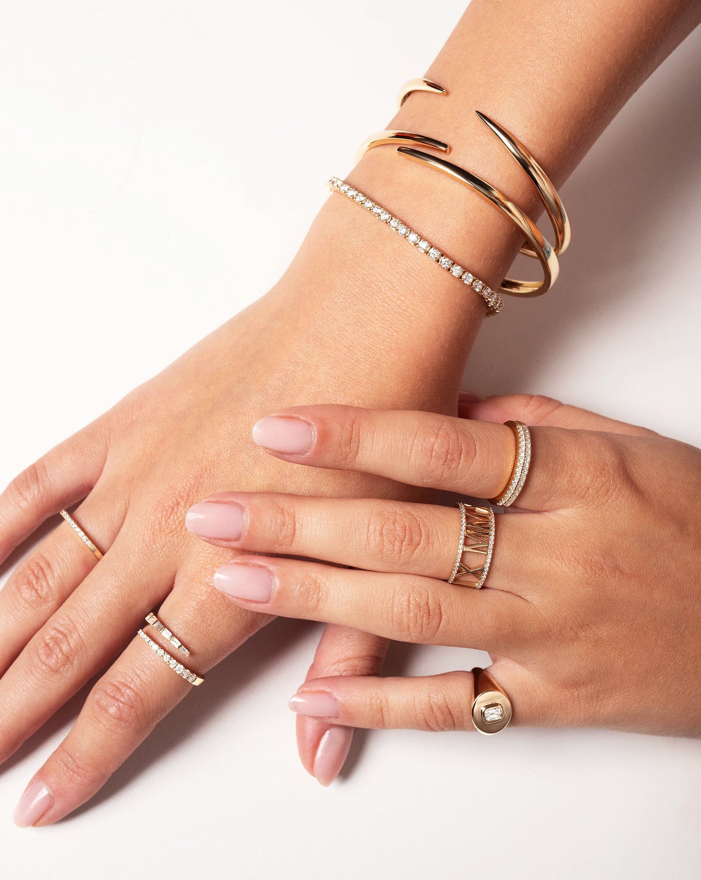 Luxe Open Diamond Wrap Ring worn on pointer finger along with the Stackable Pave Diamond Ring on ring finger. On other hand model is wearing the Diamond Signet Pinky Ring, Personalized Diamond Roman Numeral Ring. Model is also wearing the Gold Claw Cuff, Open Gold Wrap Bangled and the Classic Diamond Tennis Bracelet.