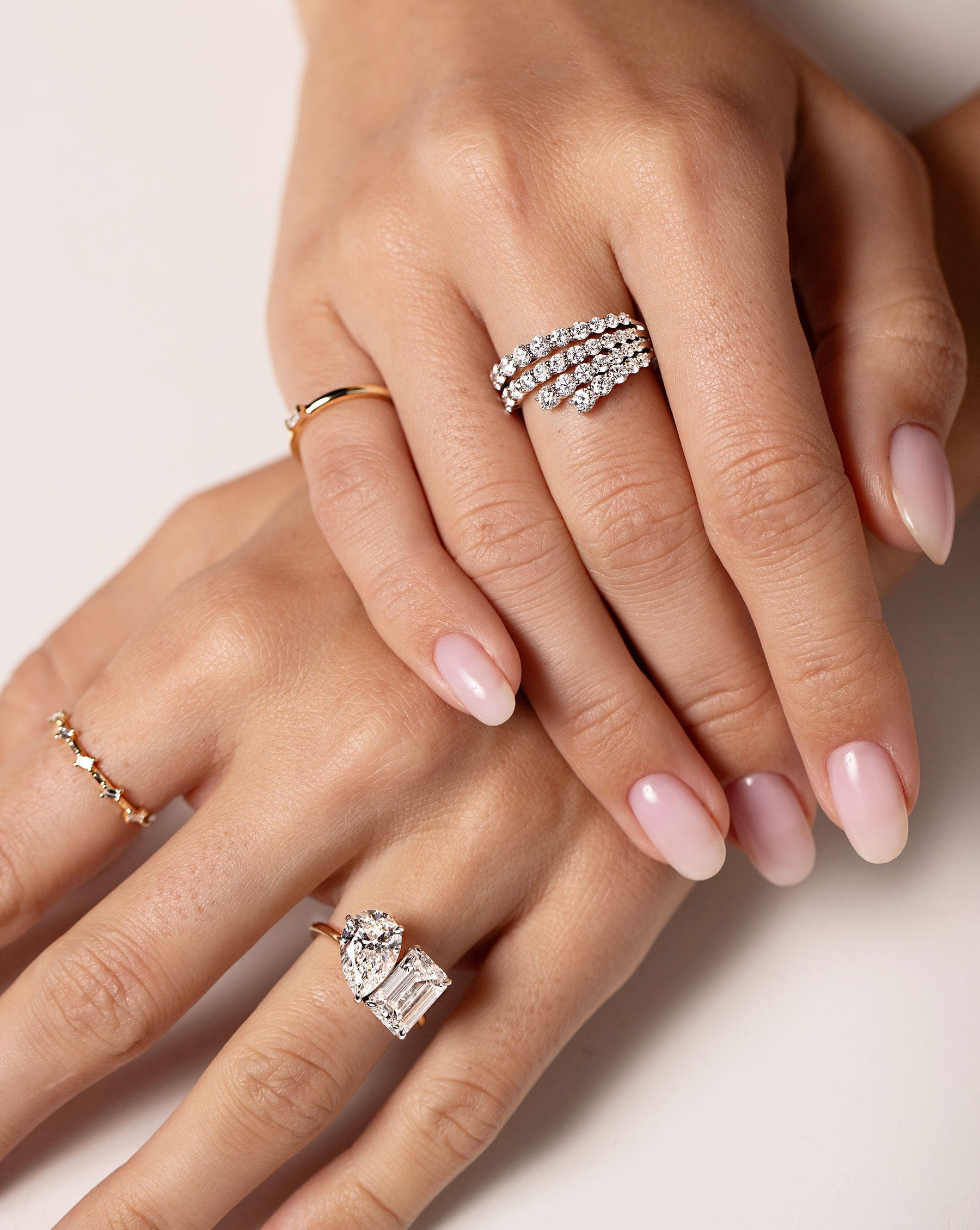 Close up image of the Fanned Diamond Statement Ring on hand of model along with the Single Baguette Diamond Ring, Baguette Distance Ring, and a Toi et Moi Engagement Ring