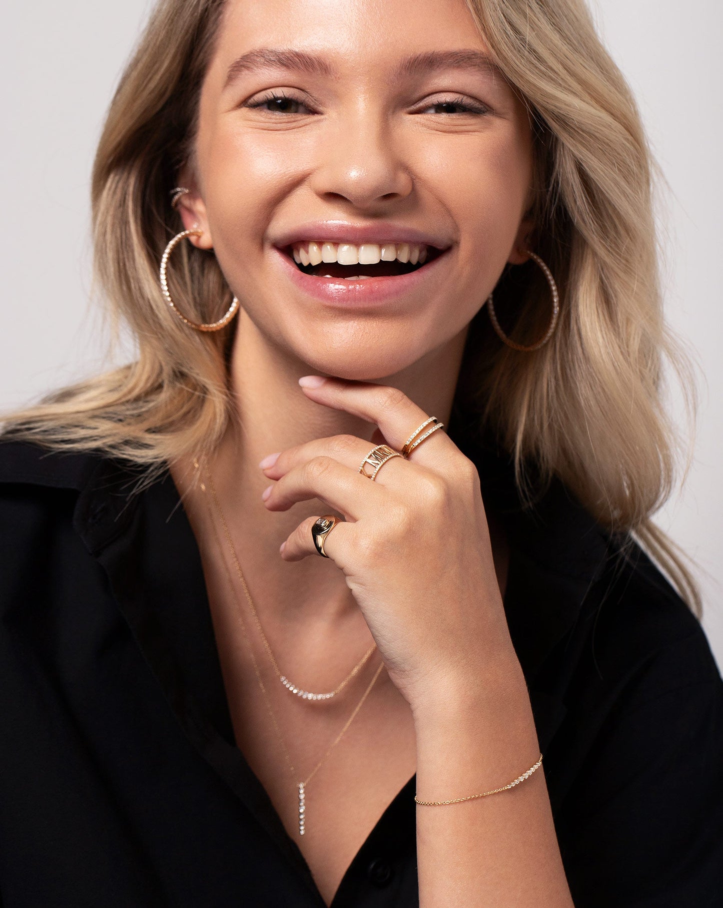 Diamond Roman Numeral Personalized Ring worn with two Stackable Pave Diamond Rings and Diamond Signet Pinky Ring on hand of model. Model is also wearing the Vertical Graduated Single Prong Necklace, Graduated Single Prong Necklace, Diamond Eternity Hoops and the Graduated Single Prong Diamond Bracelet.