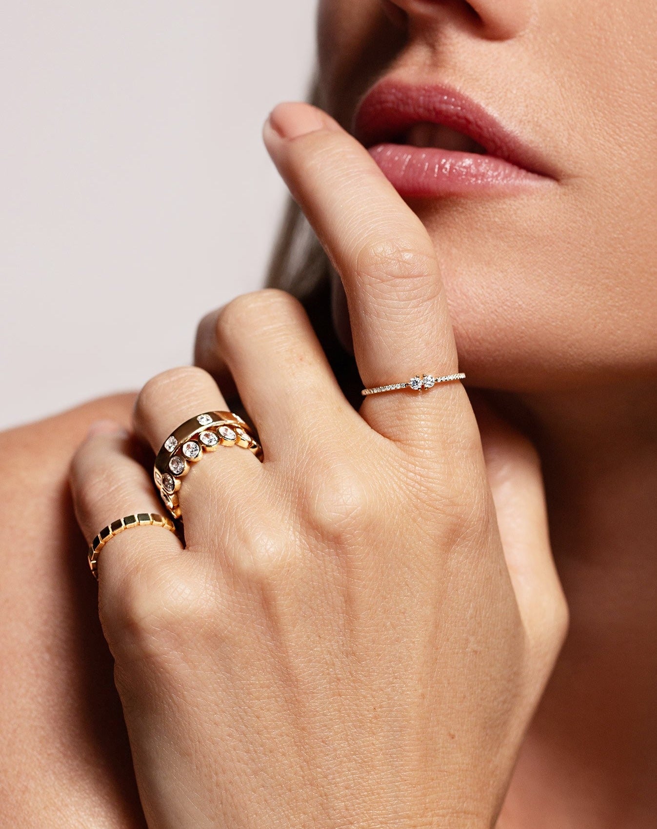 Twin diamond ring, bezel-set oval diamond eternity band, gold band with inlay round diamonds, and gold geometric ring shown on model