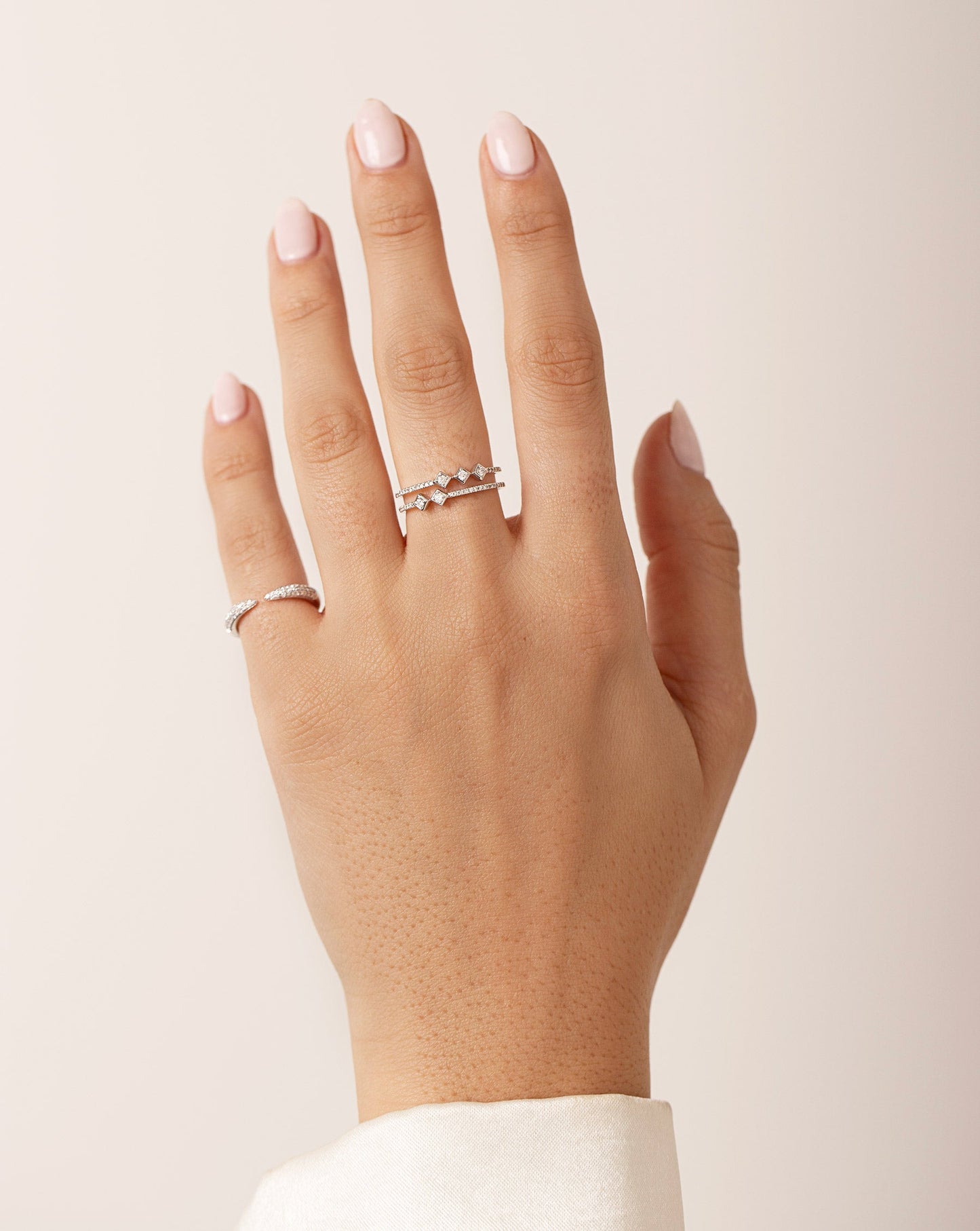 Model hand wearing asymmetrical stacked diamond ring and triple row diamond claw ring
