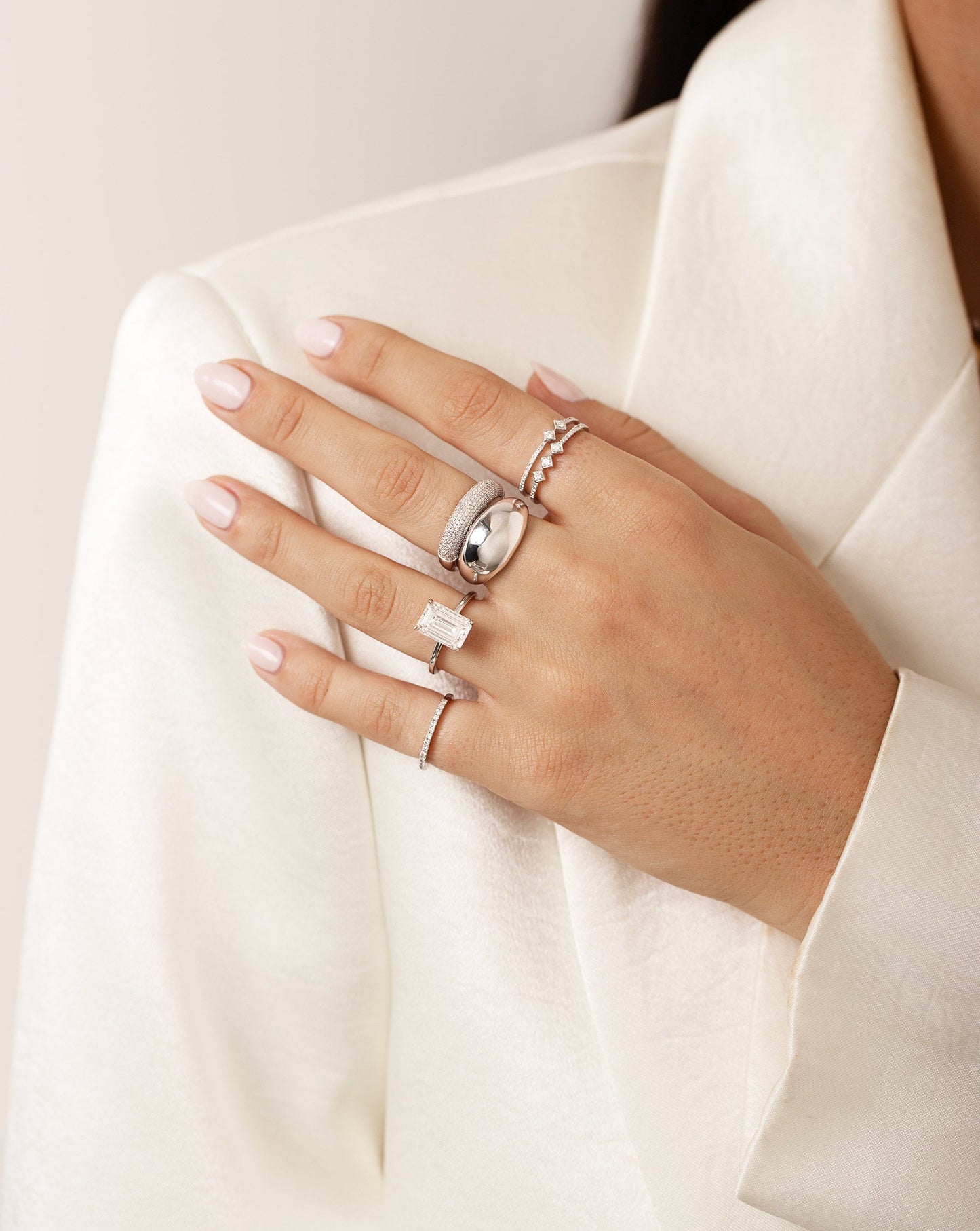 Model with hand touching shoulder wearing white blazer and 5 rings