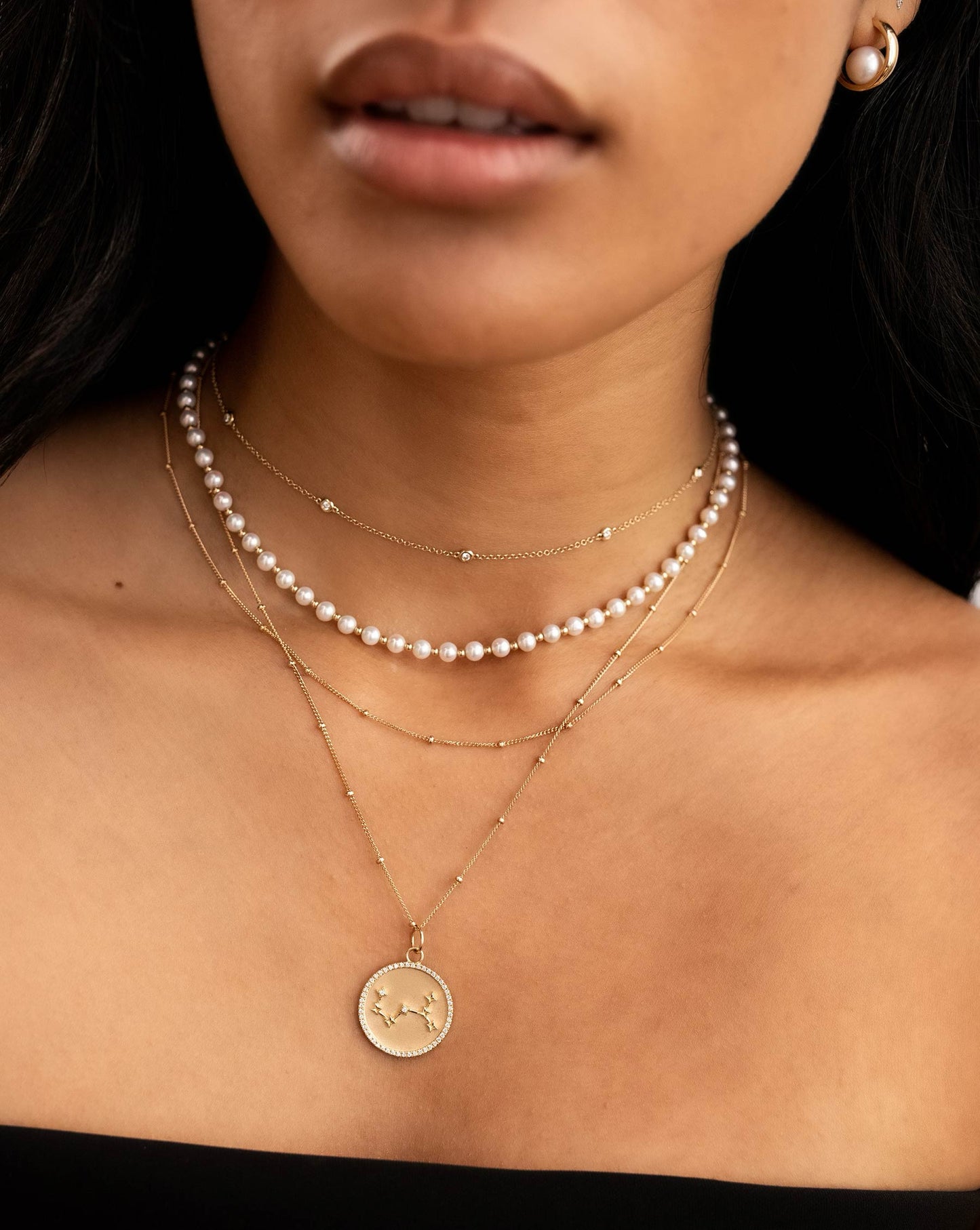 bezel set round diamond station necklace, round pearl and gold bead choker necklace, gold bead station necklace, and zodiac medallion pendant necklace on model