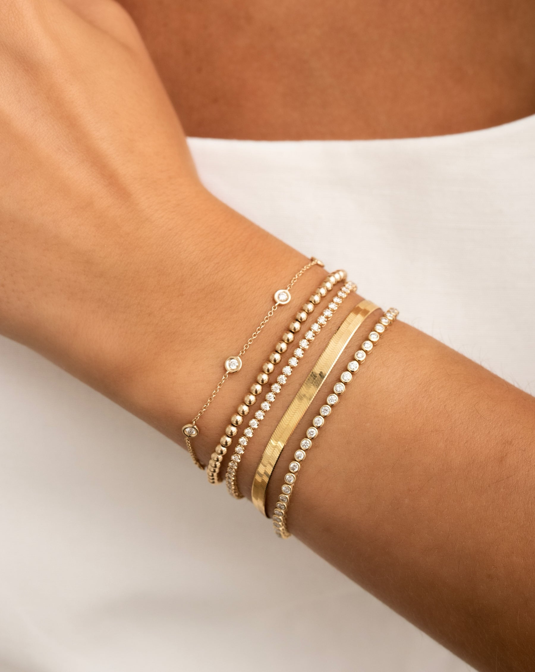 bezel-set diamond station bracelet, gold beaded bracelet, mini diamond tennis bracelet, gold herringbone bracelet, bezel-set round diamond tennis bracelet on model