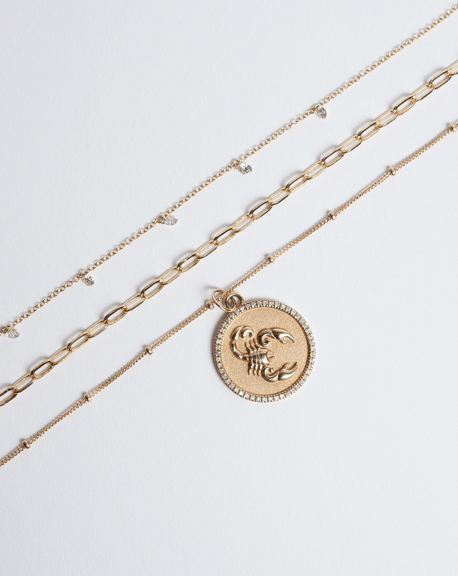 Flat lay of Zodiac Medallion Necklace and 2 other gold necklaces
